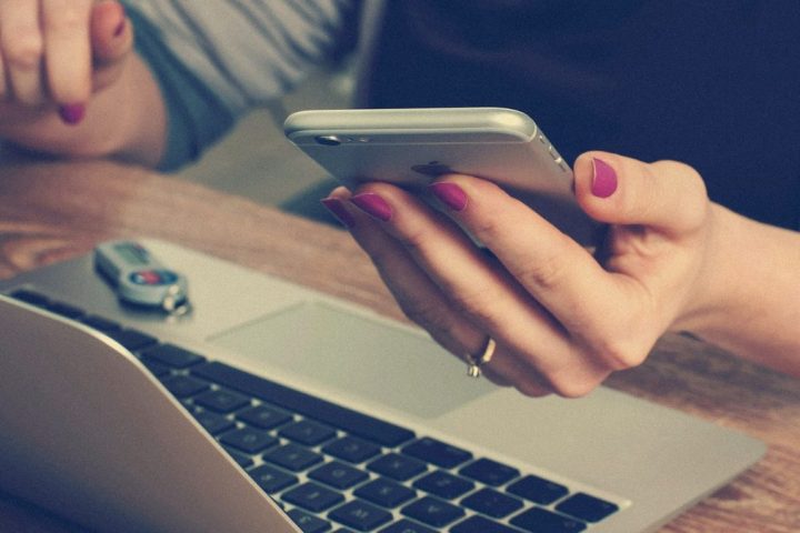 Mâini verificând cifre pe telefon, lângă un laptop deschis