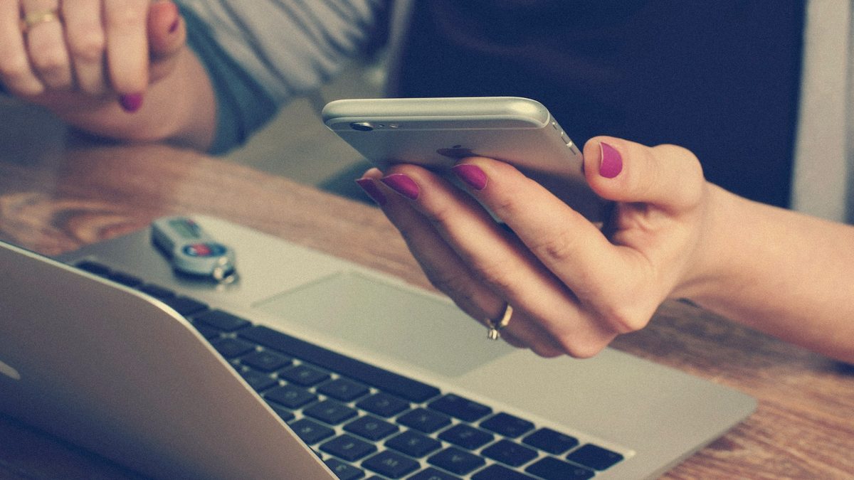 Mâini verificând cifre pe telefon, lângă un laptop deschis