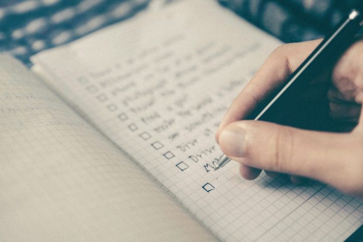 Mână bifând punctele unei liste de verificare într-un carnet