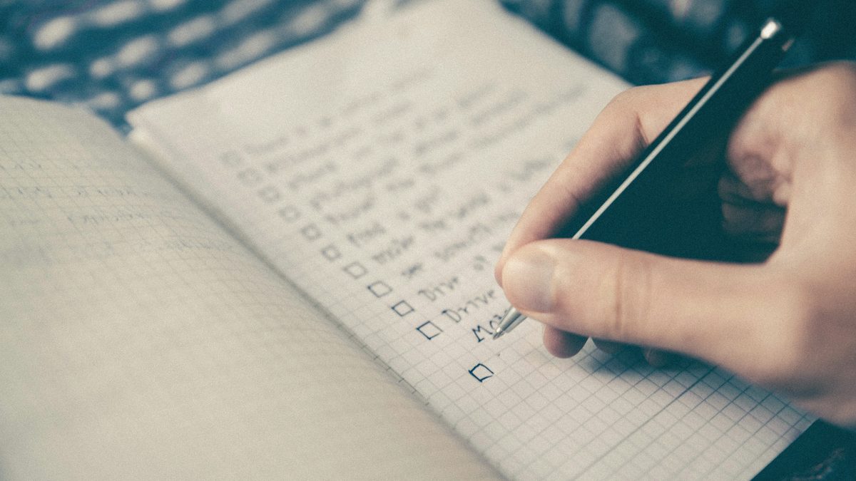 Mână bifând punctele unei liste de verificare într-un carnet